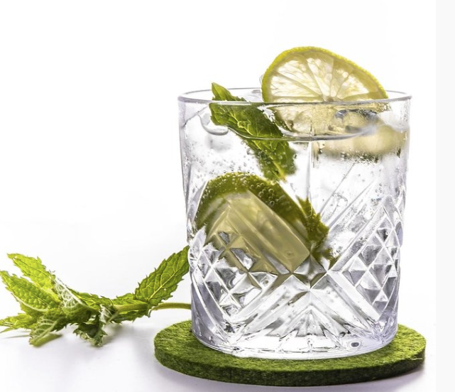 Clear glass with lime slices on green wool felt coaster with mint garnish
