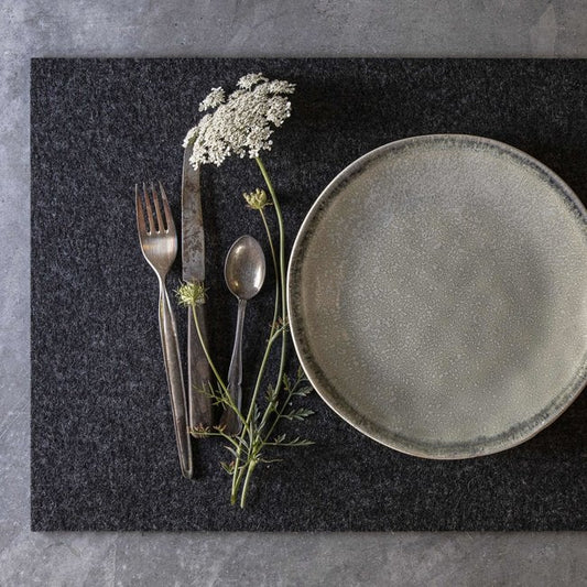 Dining setup with plate, cutlery, and flowers on dark grey wool felt placemat over light grey base