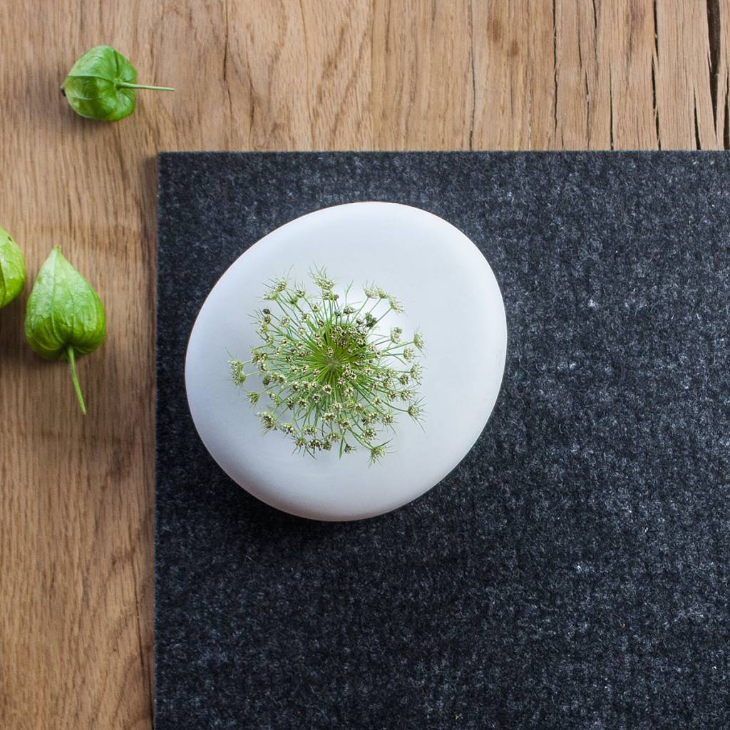 White plate with garnish on dark grey wool felt placemat over wooden table