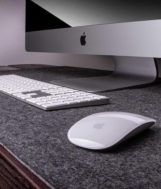 Apple iMac setup on dark grey wool felt desk pad with white keyboard and mouse