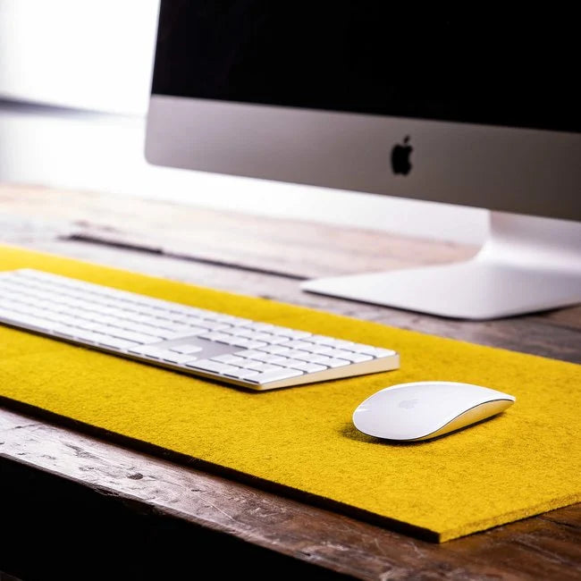iMac with white keyboard and mouse on bright yellow wool felt desk pad on wooden table